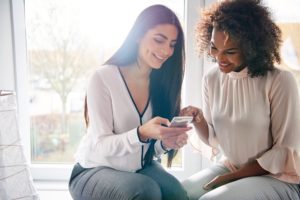 Two smiling women surfing internet with smartphone